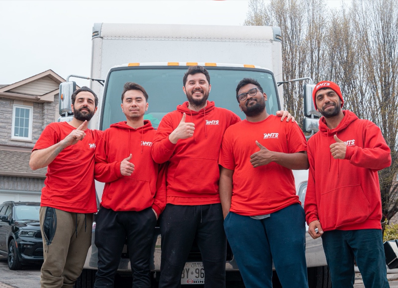 The MTS Moving crew in front of their truck, all in red MTS hoodies giving thumbs up